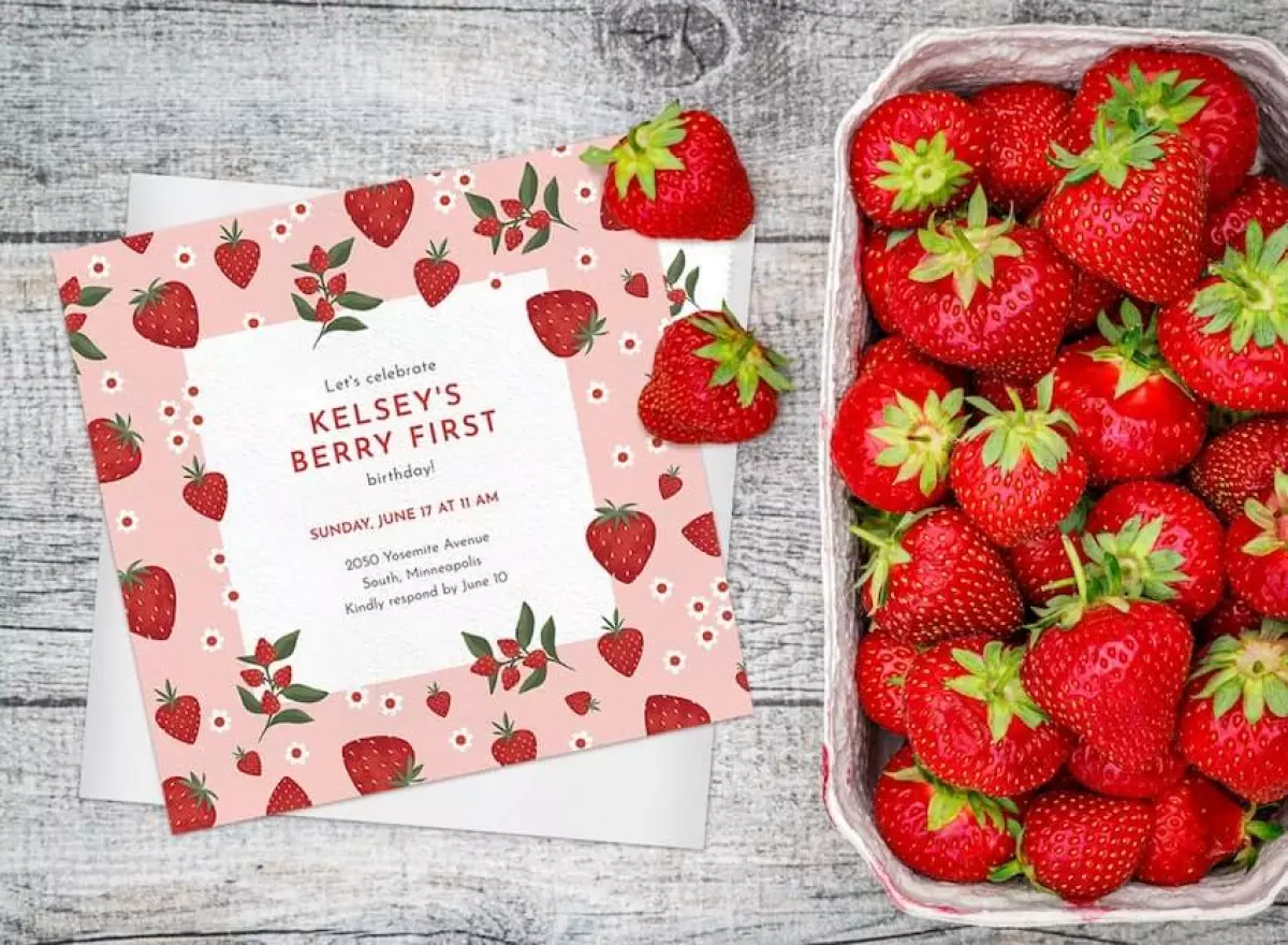 Berry first birthday: strawberry themed invitation and a bowl of strawberries on the side